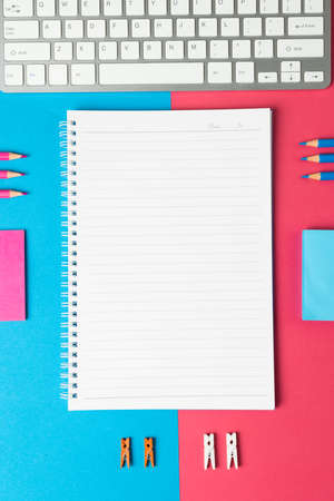 Vertical composition of notebook with copy space and school equipment on blue and pink surface. School equipment, tools, learning and creativity concept.の写真素材