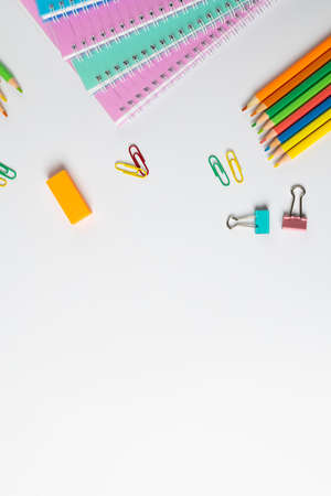 Vertical composition of notebooks, clips and crayons on white surface with copy space. School...