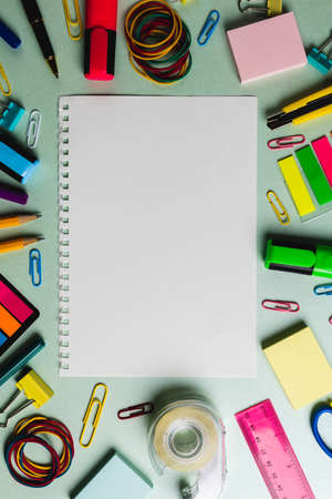 Vertical composition of notebook with copy space and frame made of school tools on green surface....