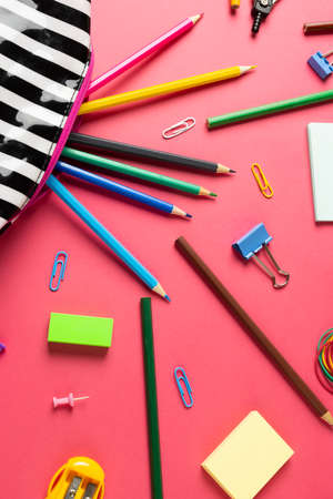 Vertical composition of crayons in striped case, clips and sharpener on pink surface. School equipment, tools and creativity concept.の写真素材