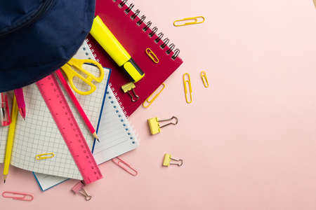 Composition of notebooks and school equipment in navy case on pale pink surface. School equipment,...