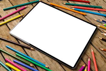 Composition of tablet with copy space and crayons on wooden surface. School equipment, tools,...