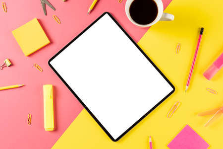 Composition of tablet with copy space, coffee and school items on pink and yellow surface. School equipment, tools, learning with technology and creativity concept.の写真素材