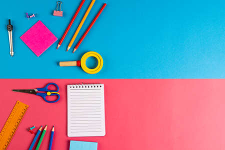 Composition of colorful school equipment with notebook on blue and pink surface. School equipment,...