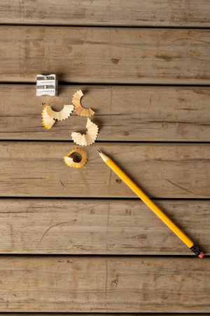 Vertical image of pencil, sharpener and peelings on wooden background. School equipment, tools,...