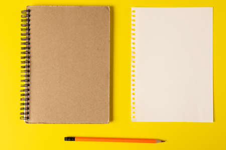 Composition of notebooks with copy space and pencil on yellow surface. School equipment, tools,...