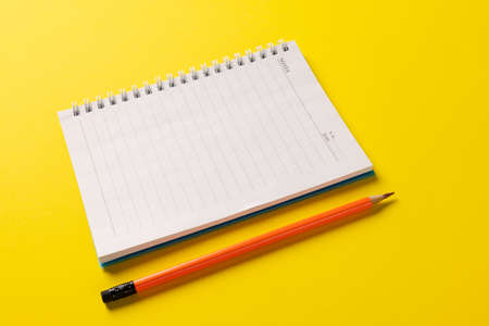 Composition of notebook with copy space and pencil on yellow surface. School equipment, tools,...