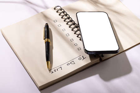 Image of notebook with to do list, pen and smartphone with copy space on white surface. Business, working in office, equipment and tools concept.の写真素材