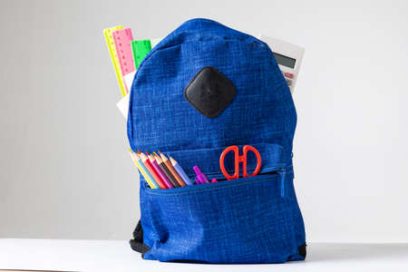 Vertical image of backpack with school equipment on white surface. School equipment, tools, learning...
