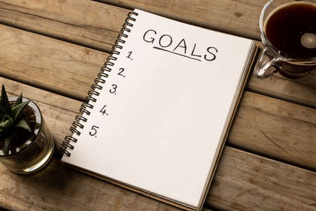 Image of notebook with goals and copy space on wooden surface with coffee. Business, tasks, office...