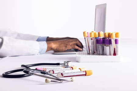 Vials with monkeypox virus and stethoscope over african american male doctor using laptop. Monkeypox...