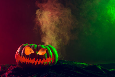 Composition of halloween carved pumpkin with smoke, green and red light on black background. Halloween tradition and celebration concept.の写真素材