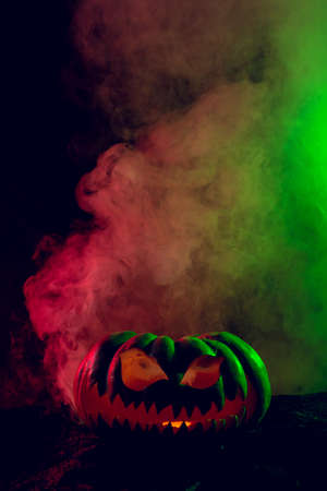 Composition of halloween carved pumpkin with smoke, green and red light on black background. Halloween tradition and celebration concept.の写真素材