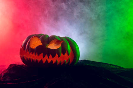 Composition of halloween carved pumpkin with smoke, green and red light on black background. Halloween tradition and celebration concept.の写真素材