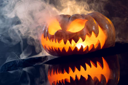 Composition of halloween carved pumpkin with smoke and orange light on black background. Halloween...