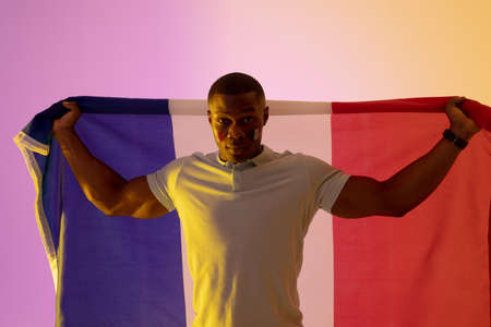Portrait of happy african american male supporter with flag of france over pink lighting. Sport, movement, training and active lifestyle concept.の写真素材