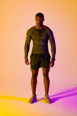 Portrait of african american male runner with sportswear over pink lighting. Sport, movement,...