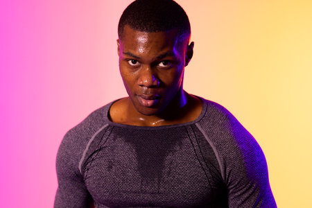 Portrait of african american male runner with sportswear over pink lighting. Sport, movement,...