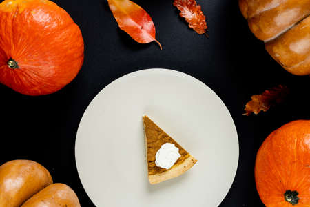 Composition of piece of pumpkin pie on plate and leaves with pumpkins on black background. Halloween, autumn, tradition and celebration concept.の写真素材