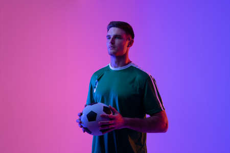 Caucasian male soccer player with football over neon pink lighting. Sport, movement, training and active lifestyle concept.の写真素材