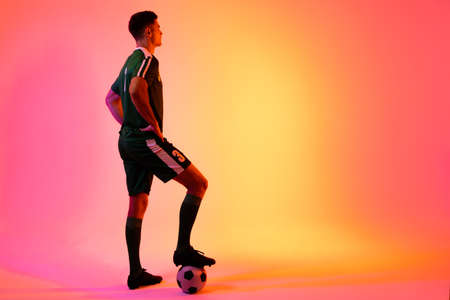 Caucasian male soccer player with football over neon pink lighting. Sport, movement, training and active lifestyle concept.の写真素材