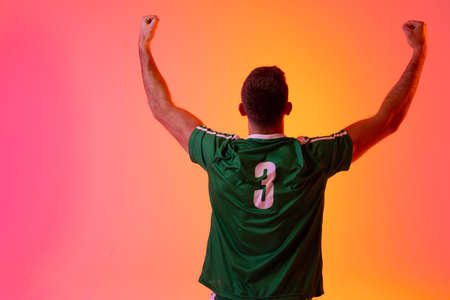 Caucasian male soccer player raising hands over neon pink lighting. Sport, movement, training and active lifestyle concept.の写真素材