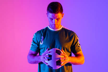 Caucasian male soccer player with football over neon pink lighting. Sport, movement, training and...