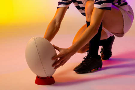 Caucasian female rugby player crouching with rugby ball over neon pink lighting. Sport, movement, training and active lifestyle concept.の写真素材