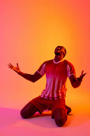 Happy african american male soccer player raising hands over neon pink lighting. Sport, movement, training and active lifestyle concept.の写真素材