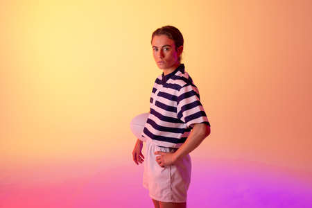 Portrait of caucasian female rugby player with rugby ball over neon pink lighting. Sport, movement, training and active lifestyle concept.の写真素材