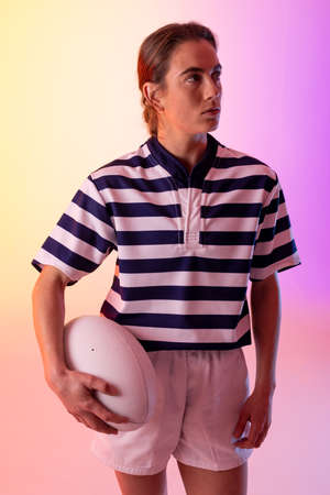 Caucasian female rugby player with rugby ball over neon pink lighting. Sport, movement, training and active lifestyle concept.の写真素材