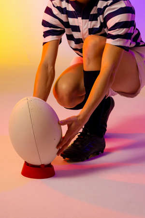 Caucasian female rugby player crouching with rugby ball over neon pink lighting. Sport, movement, training and active lifestyle concept.の写真素材