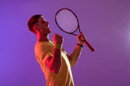 Happy caucasian male tennis player with tennis racket over neon pink lighting. Sport, movement, training and active lifestyle concept.の写真素材