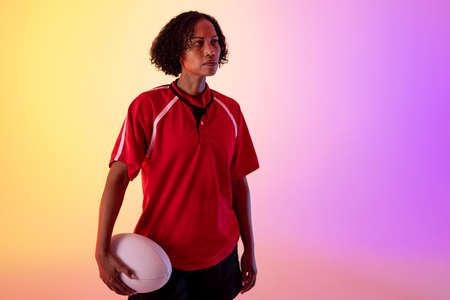 African american female rugby player with rugby ball over neon pink lighting. Sport, movement, training and active lifestyle concept.の写真素材