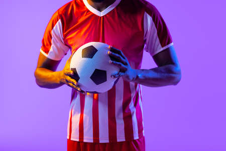 African american male soccer player with football over neon pink lighting. Sport, movement, training and active lifestyle concept.の写真素材