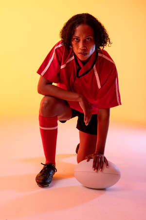 Portrait of african american female rugby player with rugby ball over neon yellow lighting. Sport, movement, training and active lifestyle concept.の写真素材