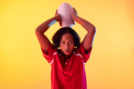 Portrait of african american female rugby player with rugby ball over neon yellow lighting. Sport, movement, training and active lifestyle concept.の写真素材