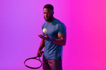 Image of african american male tennis player in violet and pink neon lighting. Sport, movement, fitness and active lifestyle concept.の写真素材