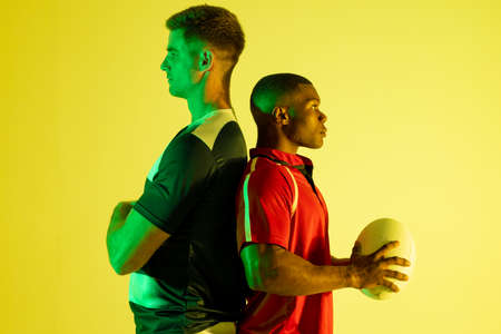 Diverse male rugby players with rugby ball over yellow lighting. Sport, movement, training and active lifestyle concept.の写真素材