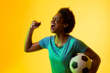 Image of african american female soccer fan with flag of portugal cheering in yellow lighting....