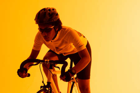 Image of african american female cyclist riding bike in yellow lighting. Sport, movement, fitness and active lifestyle concept.の写真素材
