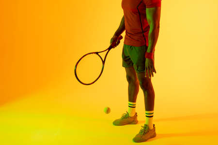 Image of low section of african american male tennis player in yellow lighting. Sport, movement, fitness and active lifestyle concept.の写真素材