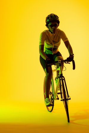 Vertical image of african american female cyclist riding bike in yellow lighting. Sport, movement, fitness and active lifestyle concept.の写真素材