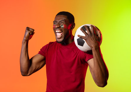 Happy african american male football supporter with flag of portugal over orange lighting. Sport, movement, training and active lifestyle concept.の写真素材