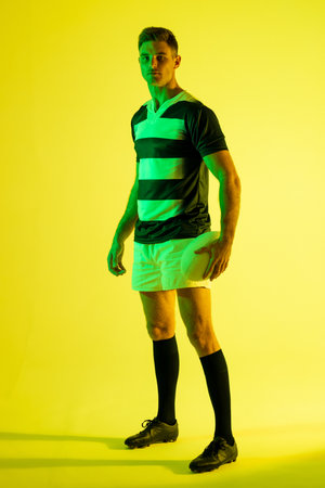 Portrait of caucasian male rugby player with rugby ball over yellow lighting. Sport, movement, training and active lifestyle concept.の写真素材