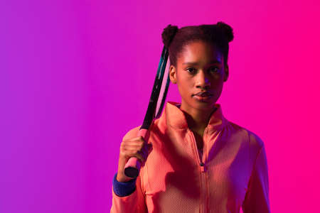 Image of african american female tennis player in violet and pink neon lighting. Sport, movement, fitness and active lifestyle concept.の写真素材