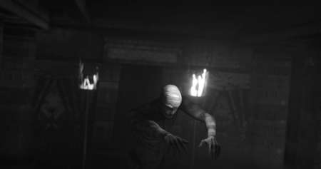 Image of scary zombie mummy walking in dark crypt with burning torches, in black and white. Halloween fear, horror and suspense concept digitally generated image.の写真素材
