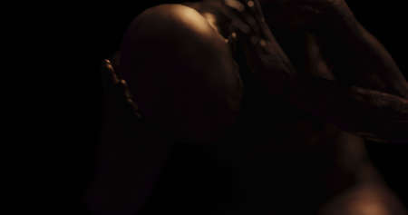 Image of distressed shirtless bald figure holding head in pain in dark room. Fear, horror and...