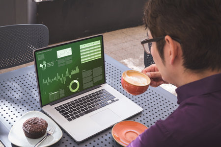 Over shoulder view of asian businessman drinking coffee, with graphs and charts on laptop screen. Business communication, working remotely and digital interface concept.の写真素材