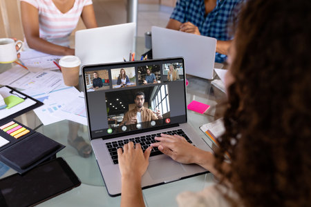 Biracial businesswoman in office making laptop video call with five diverse colleagues. Business communication, working remotely and digital interface concept.の写真素材